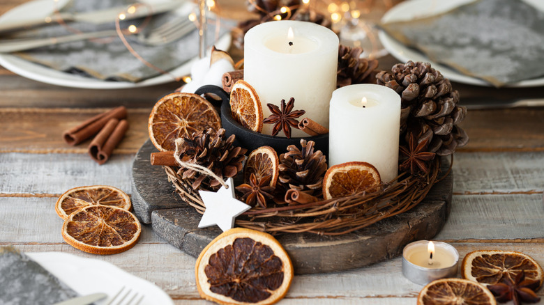 A small, rustic centerpiece with white candles, pinecones, dried citrus, and cinnamon sticks