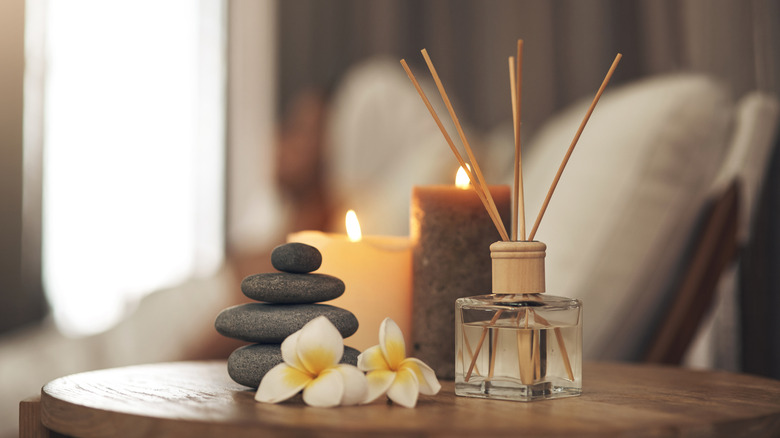 A reed diffuser, candles, and stones next to a chair.