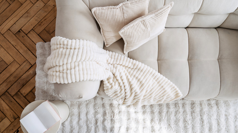 Top view of a beige couch with throw pillows, a throw blanket, and a fluffy rug nearby