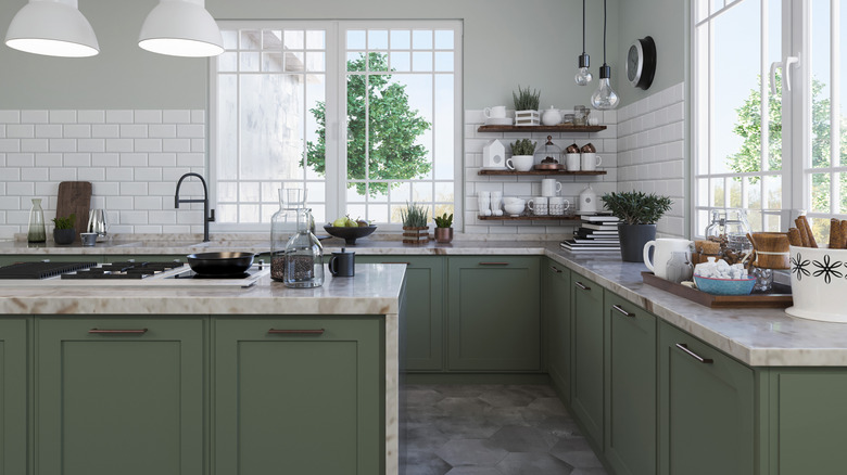 A modern kitchen with sage green cabinets, stone countertops, large windows, and white tiled backsplashes
