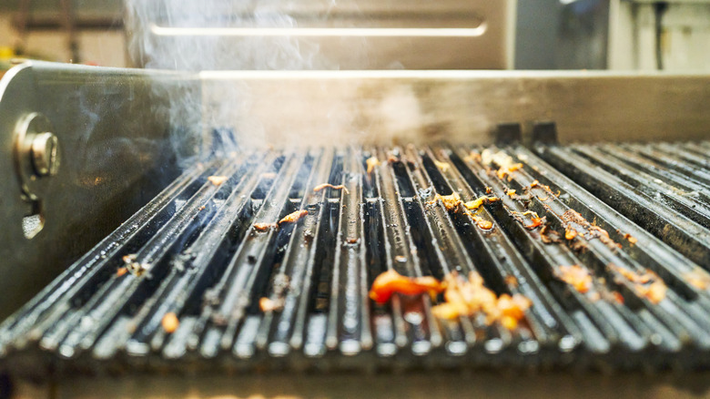 A close up of the front of a dirty grill with food debris on its surface.