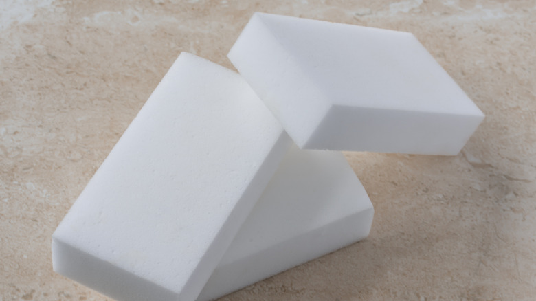 Three white melamine sponges sitting on a tan marbled countertop