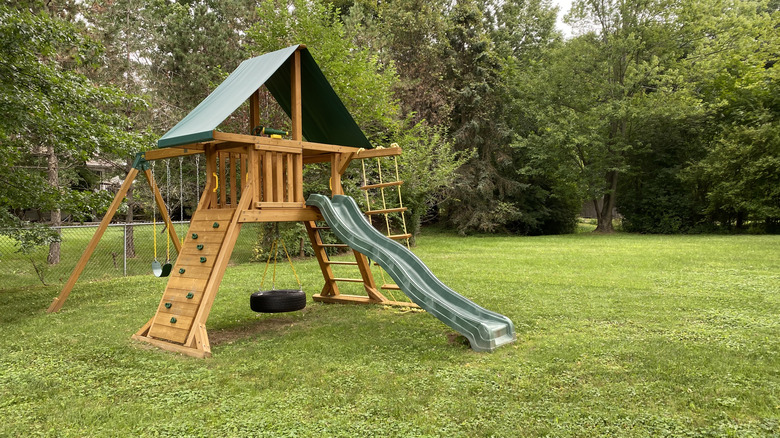 Playset with swings, climbing wall, tire swing, slide, and rope ladder, in a freshly mowed yard
