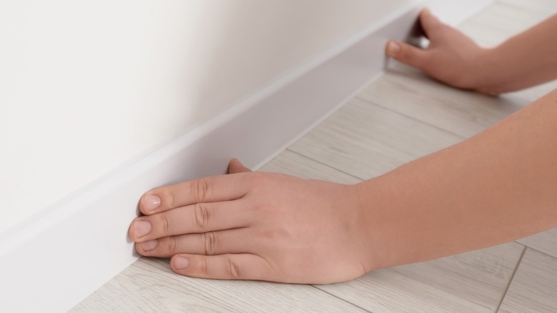 person feeling white baseboard on white wall
