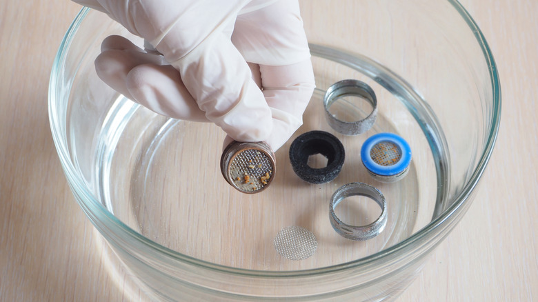 A hand is putting pieces of a faucet tip into a bowl of vinegar.