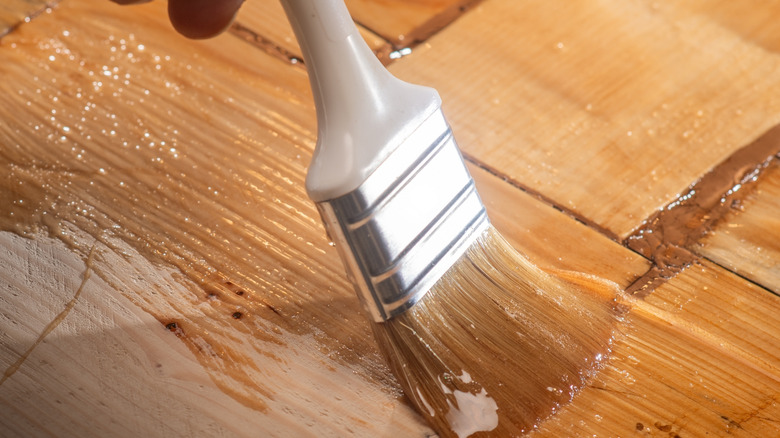 Close-up shot of a paintbrush laying a warm-toned stain on sanded wood.