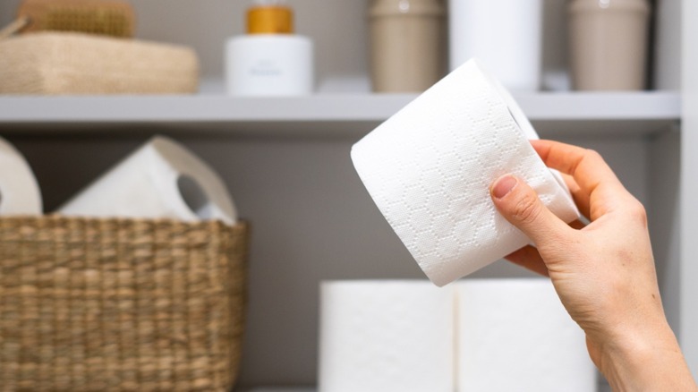person's hand putting toilet paper roll in bathroom cabinet