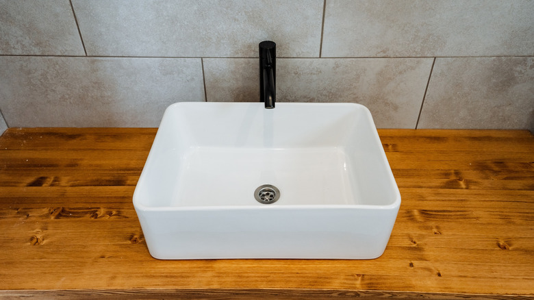A white sink on top of a stained bathroom counter with a gray patterned tile in the background
