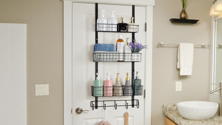 A shower caddy full of skincare products hangs on the back of the bathroom door near the vanity.