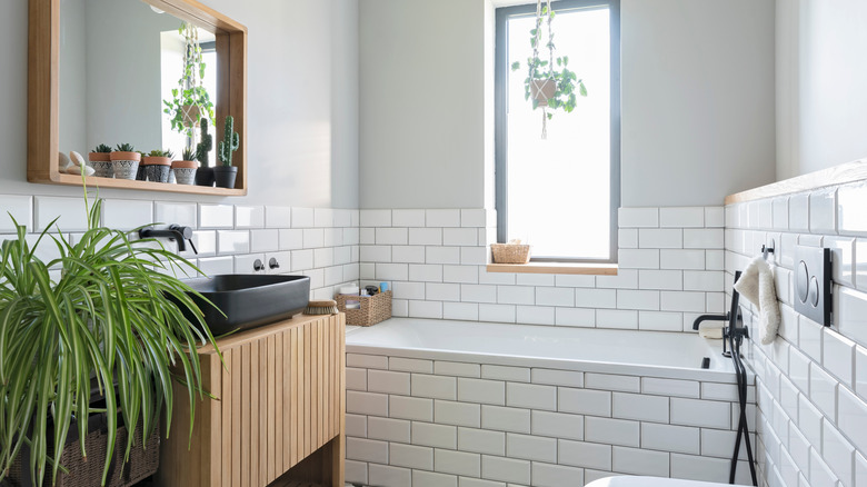 A bathroom with white tiles, a wooden under-sink cabinet, and some plants