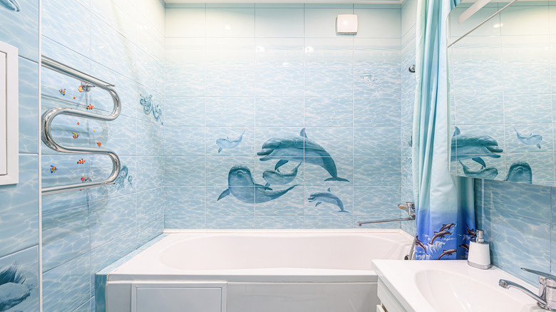 Underwater themed bathroom with a dolphin and fish art on the shower tiles, and a dolphin themed shower curtain