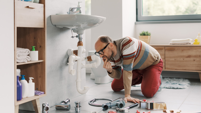 A man struggling to install drain pipes on the bathroom sink.