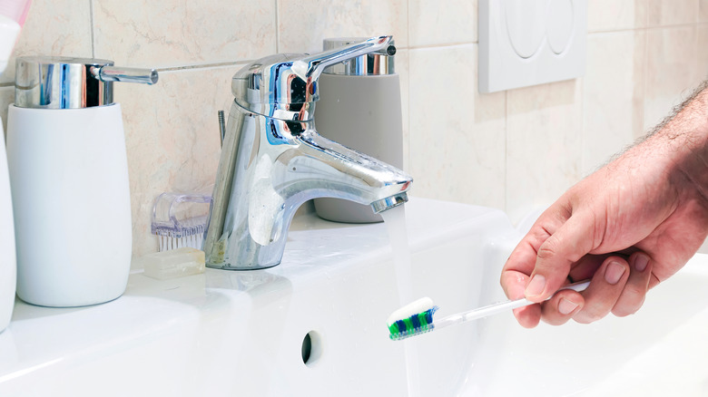Close up of person holding toothpaste on toothbrush at chrome sink faucet