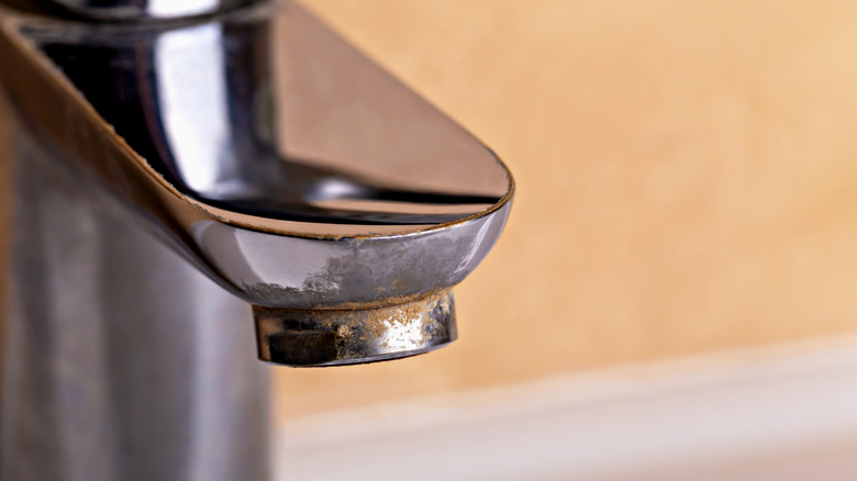 Close up of chrome sink faucet covered in limescale