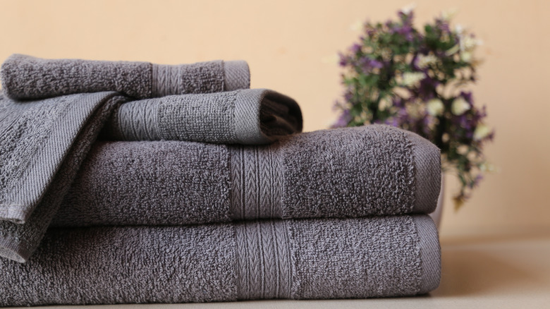 Dark grey bath towels stacked on top of each other with a purple plant in the background