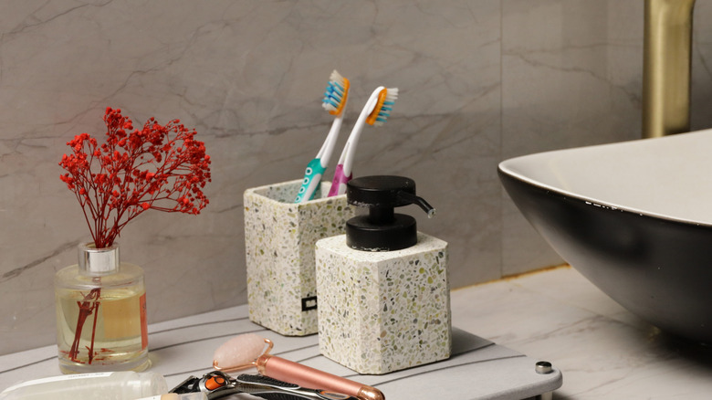 A toothbrush holder amid the accoutrement of a modern bathroom vanity contains two exposed toothbrushes