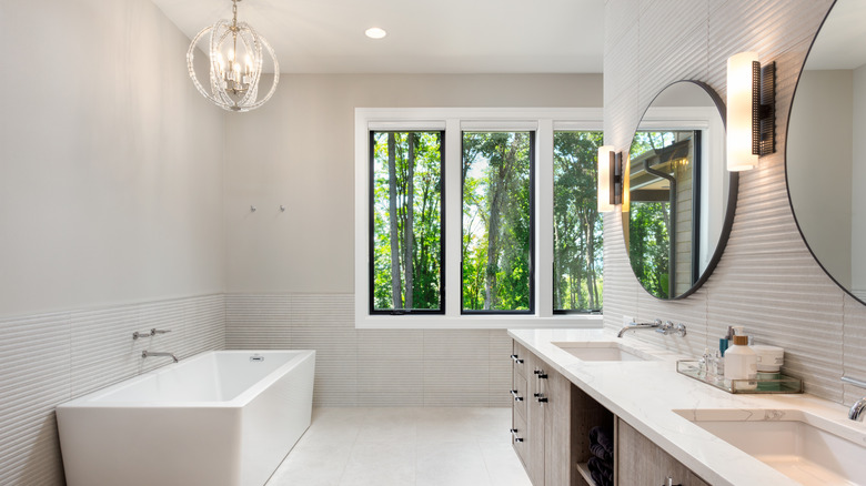 Stylish modern bathroom brightened by natural lighting, vanity scones, ceiling lights, and a pendant lamp over the tub