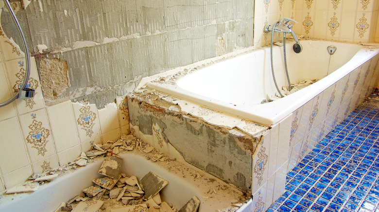 Tile is torn off the walls around a bathtub in a dated bathroom
