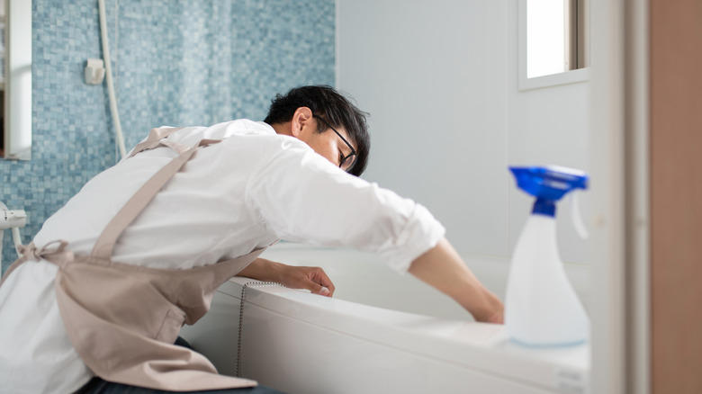 Man wearing an apron cleans the shower and tub