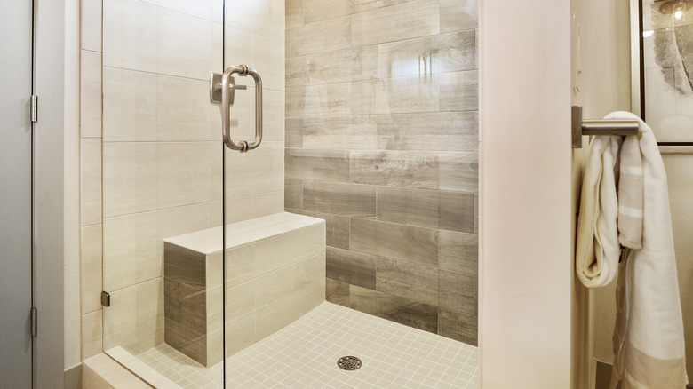 A beige shower with tile and a bench.
