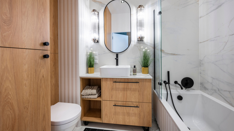 A cramped bathroom with a bulky wooden vanity crammed between the bathtub and the wall