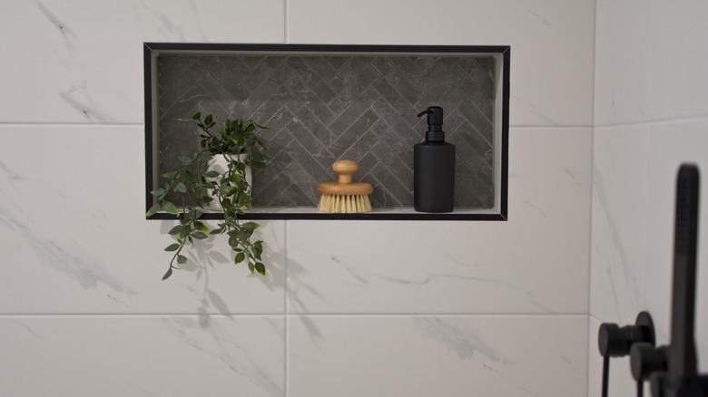 Shower wall niche tiled in black herringbone pattern with small plant, brush, and pump bottle.