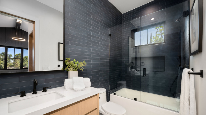 Contemporary bathroom with black tiled walls light-colored wood vanity and large mirror.