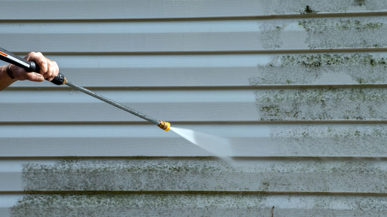 A person pressure-washes gray vinyl siding