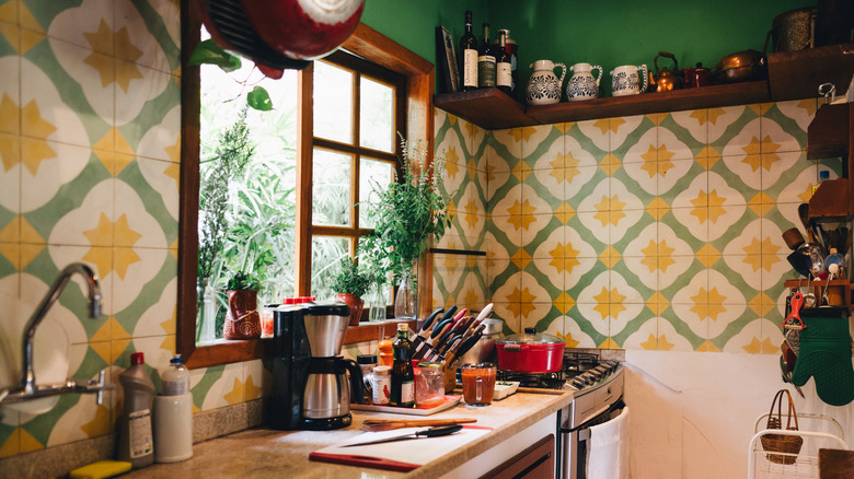 An eclectic kitchen with appliances on the counters and a colorful green and yellow tile backsplash.