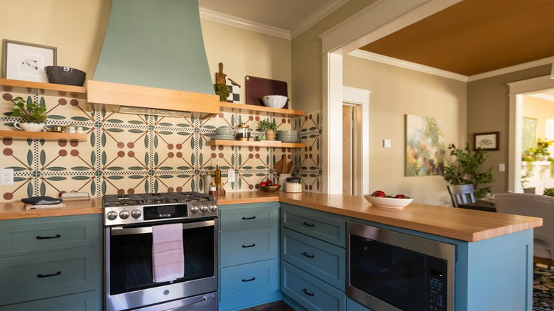 A cozy, rustic kitchen with a cherry tile backsplash, teal cabinets, and butcher block counters.