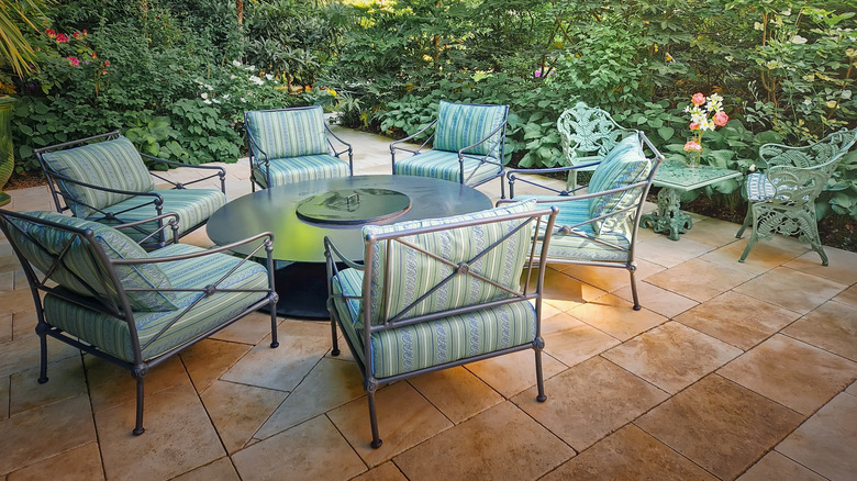 Outdoor dining set on a stone patio with greenery and flowers surrounding it