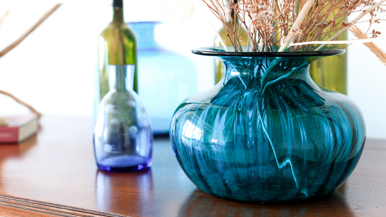 A colorful hand-blown vase sitting on a coffee table next to glass bottles