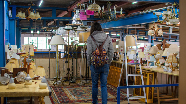 Woman from behind wearing backpack browsing vintage lamps in thrift store