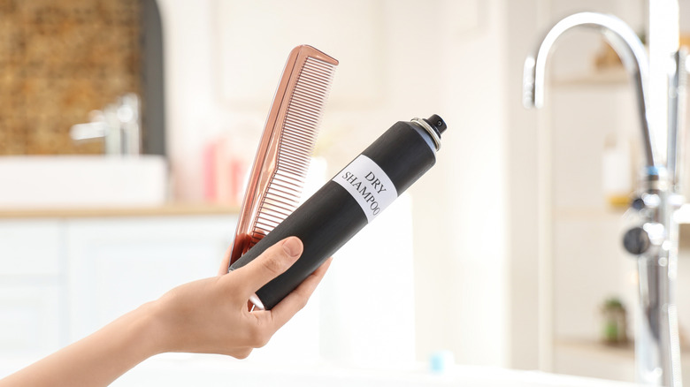 Woman's hand holding a bottle of dry shampoo and a comb