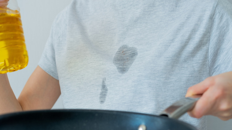 Man with grease stains on shirt holding frying pan and oil