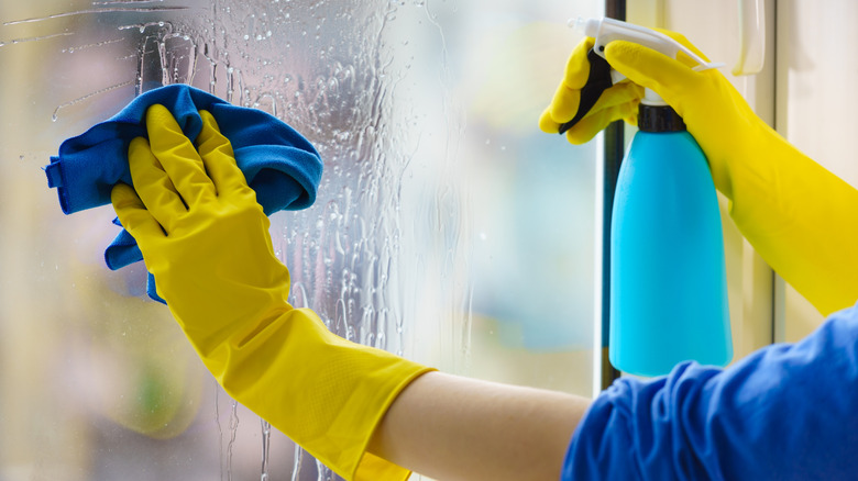 Gloved hands are cleaning a frosted glass shower door.