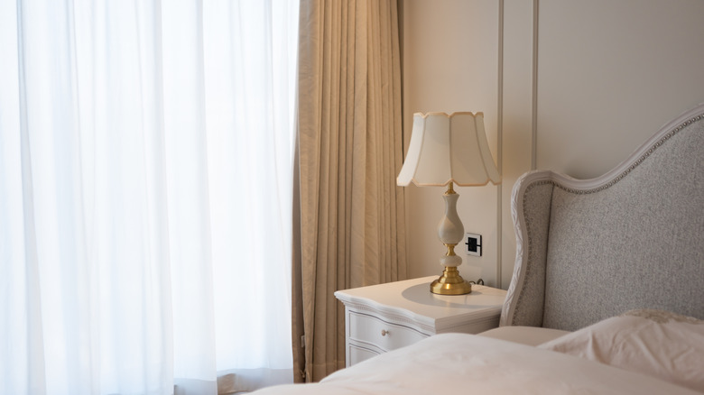 A neutral-themed bedroom, feautring a curved headboard and vintage-style lamp in white and gold.