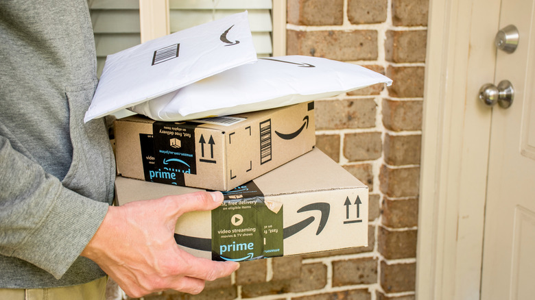 Person carrying some Amazon boxes and envelopes to a front door