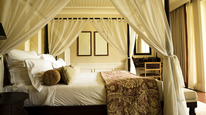 Bed with white linens and patterned throw topped with a canopy with white curtains.