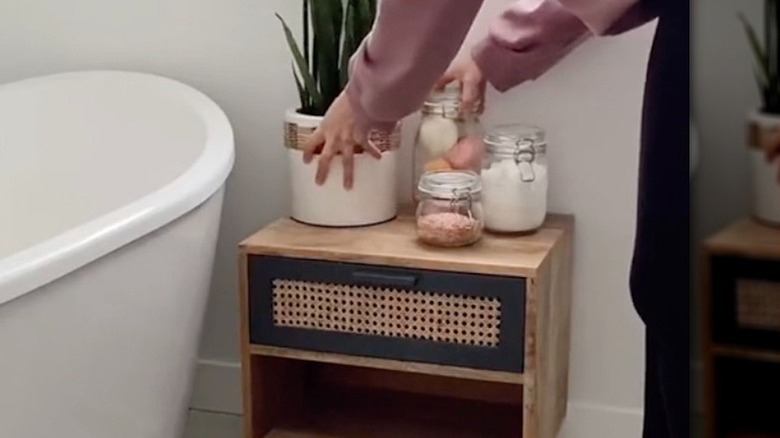 Woman using bedside table to add storage and create spa-like atmosphere in bathroom.