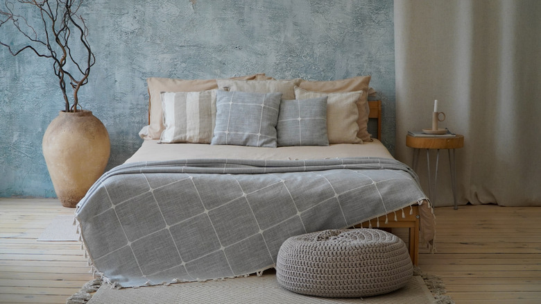 Bed with multiple pillows, round nightstand with candle, and dried twigs in a vase to the side.