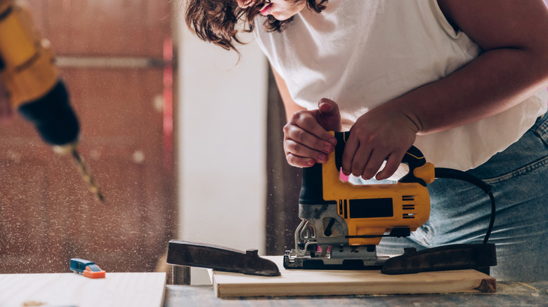 A woman cuts plywood with a jigsaw.