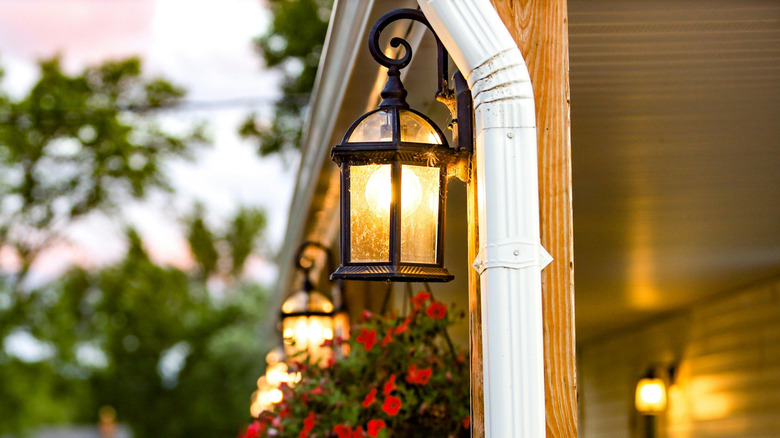 A row of outdoor lights along a porch with hanging flower baskets, with cars parked in the background.