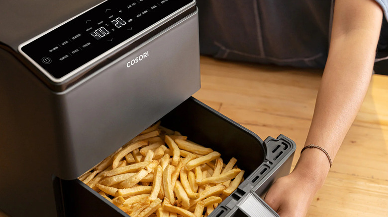 A woman opening a COSORI Dual Blaze 6.8QT air fryer with french fries inside