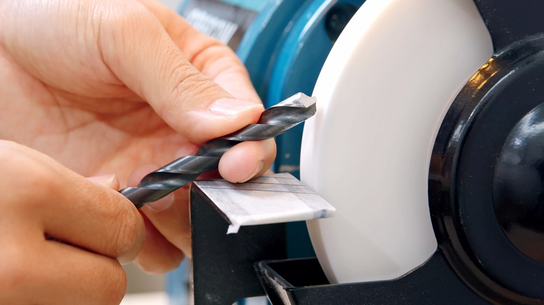 A person sharpening a drill bit on a bench grinder