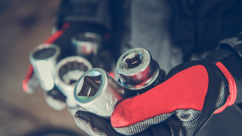 Someone wearing red and black gloves holding items designed to remove bolts.