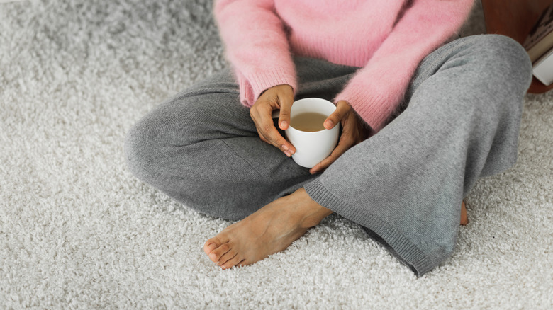 woman sitting cross-legged on wool carpet while holding cup of tea