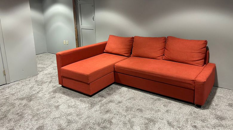 Orange sectional sofa in a carpeted basement
