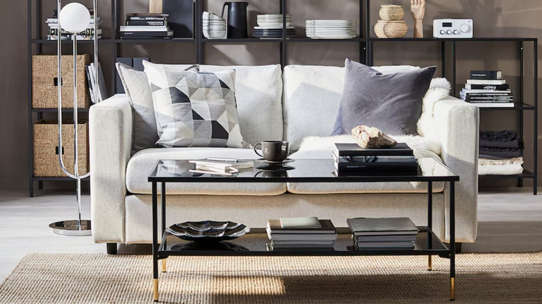 A black glass coffee table with gold feet in front of a white sofa.