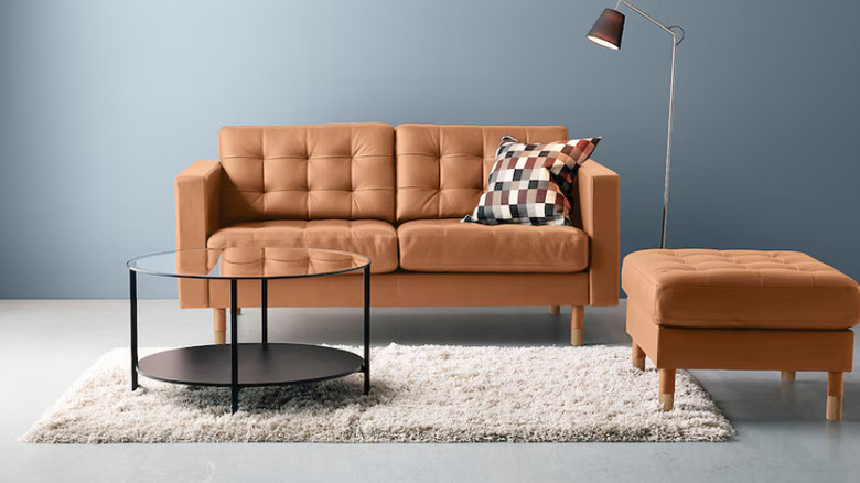 A small, black glass coffee table in front of an orange sofa.